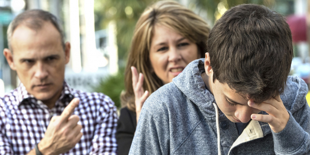 Teenage boy with head down . His parents shouting at him