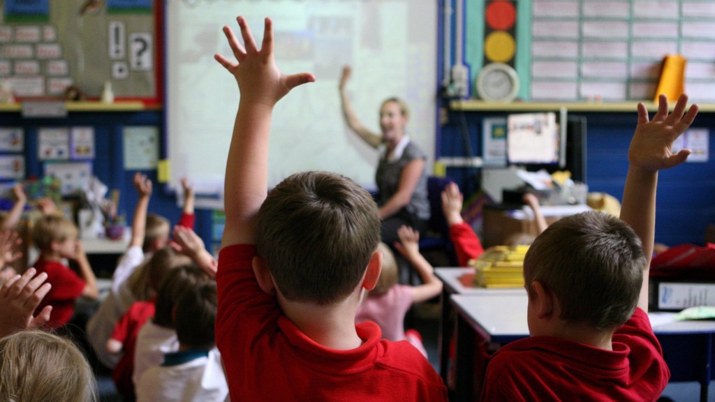 primary pupils in class with hands up