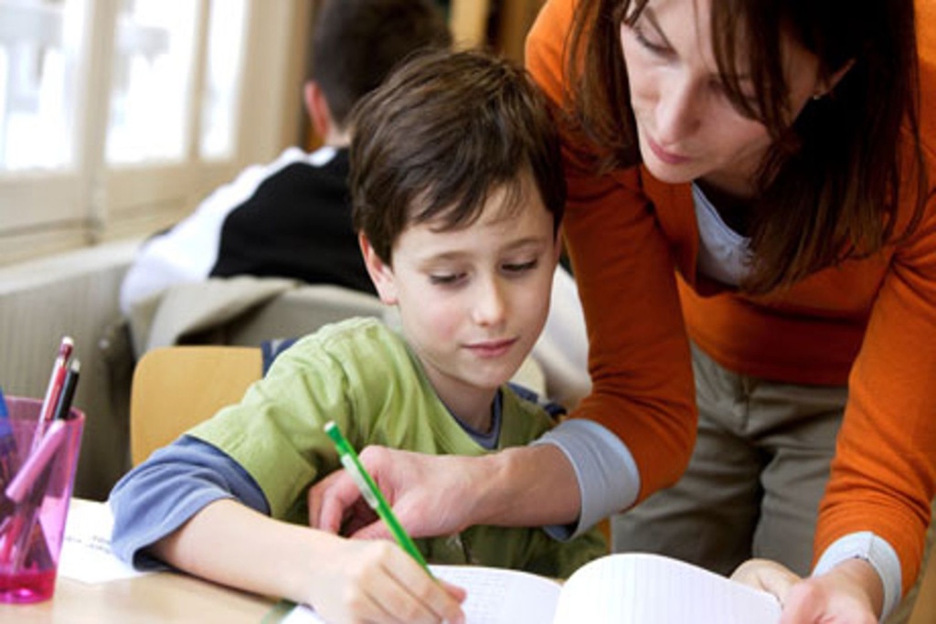 boy at desk with teacher helping him with classwork
