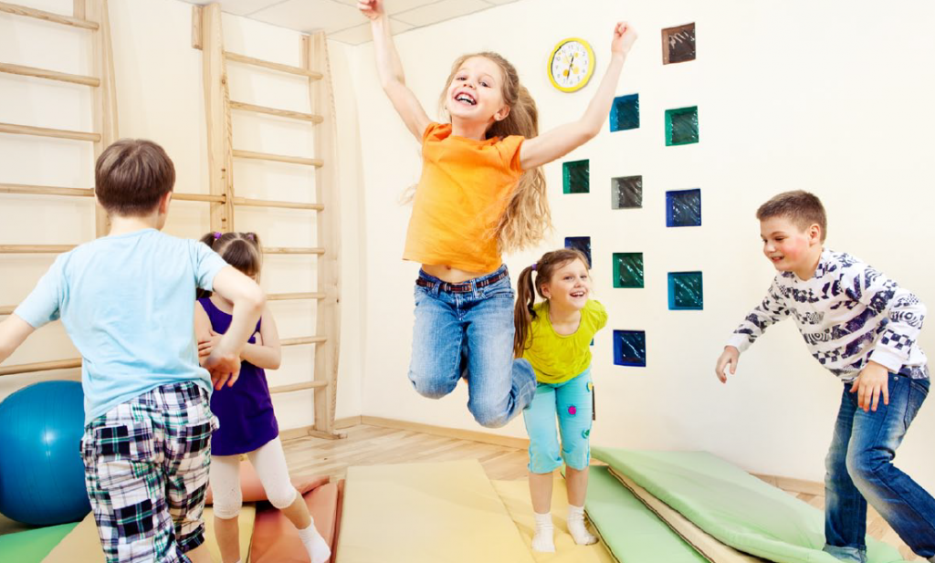 young children in gym room with girl at centre jumping high