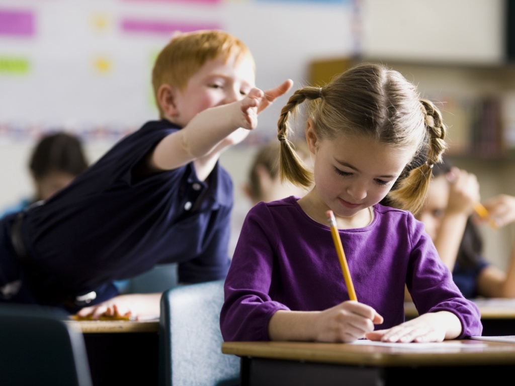 boy in class reaching to pull girls hair sitting in front of him