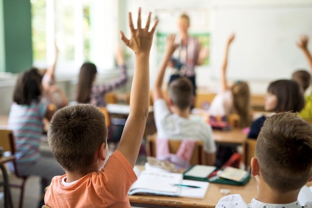 rear view of children with hands up in classroom