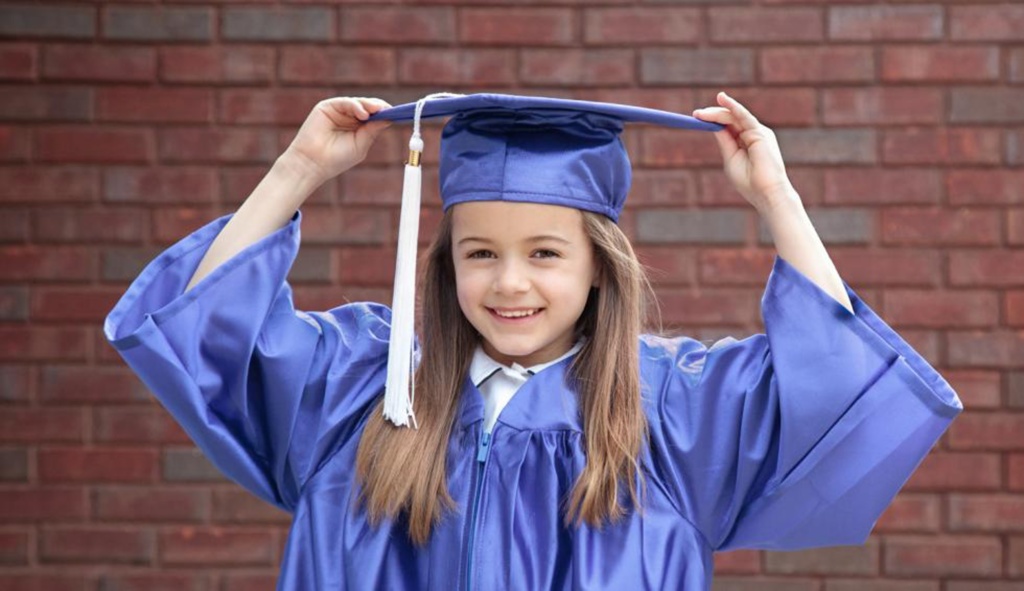 Young primary girl in graduate hat and gown