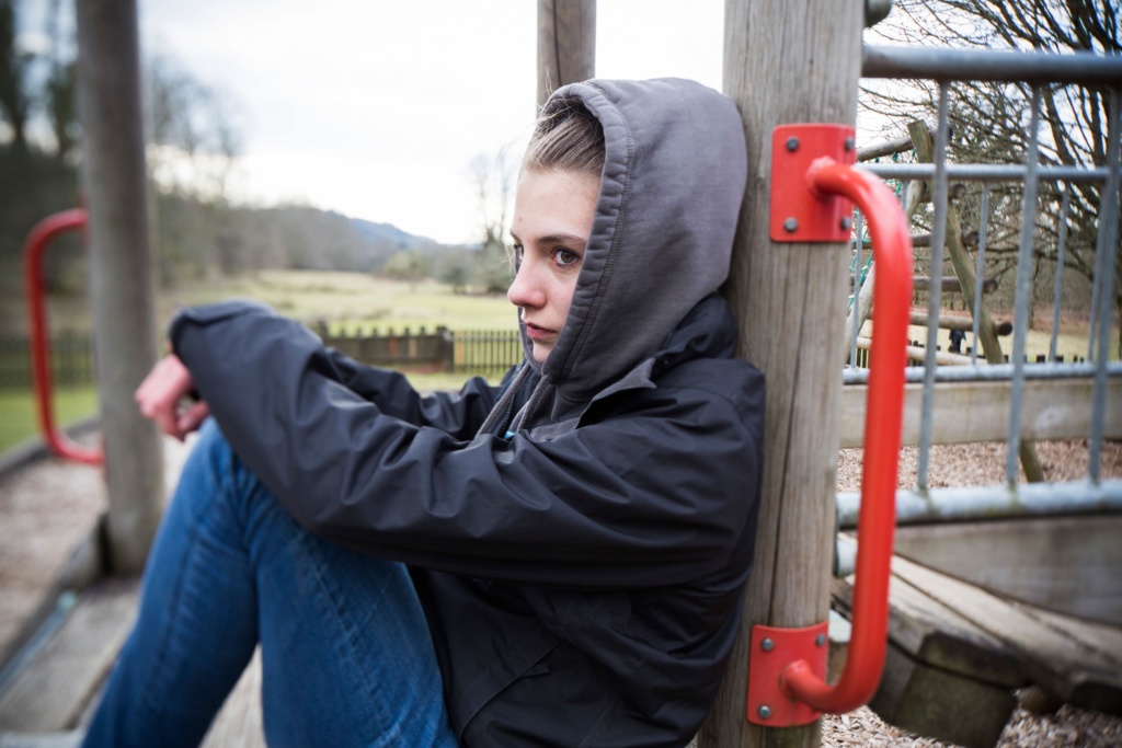 A teenage girl sitting in a children's play area looking despondent and depressed