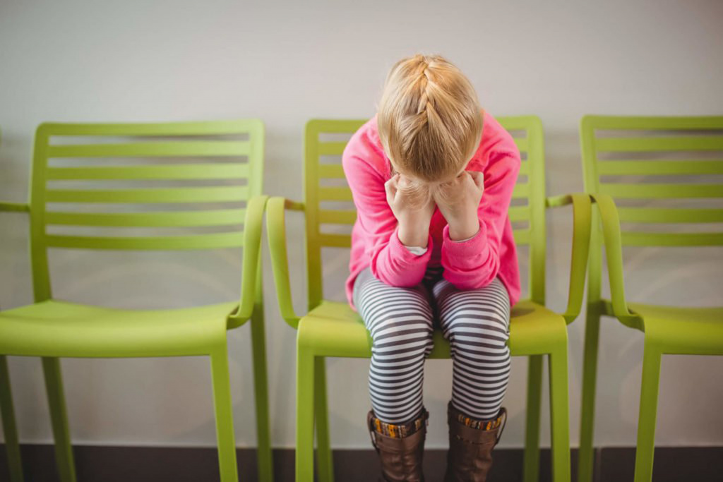 Girl sitting in green chair crouched with face in hands