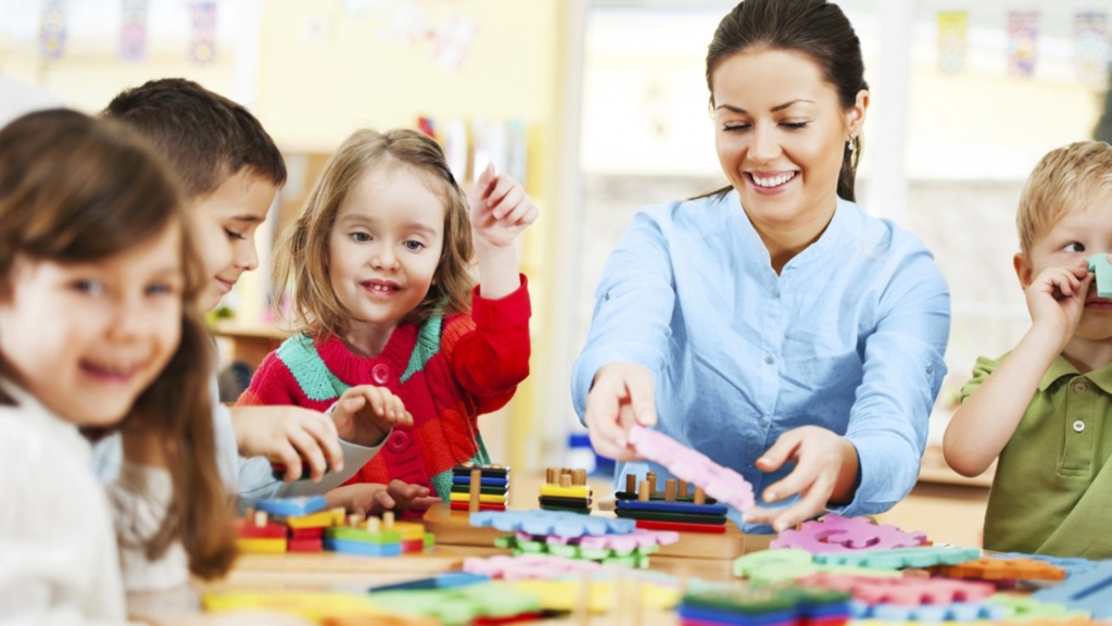 Nursery teacher with nursery children at desk doing activities