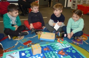 children sitting round a mat with a small wooden cube robot