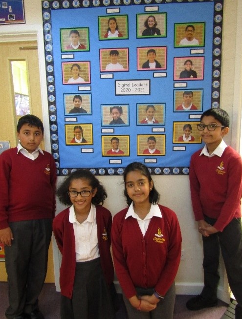 Four children in school uniform standing by a Digital Leaders Display board rom