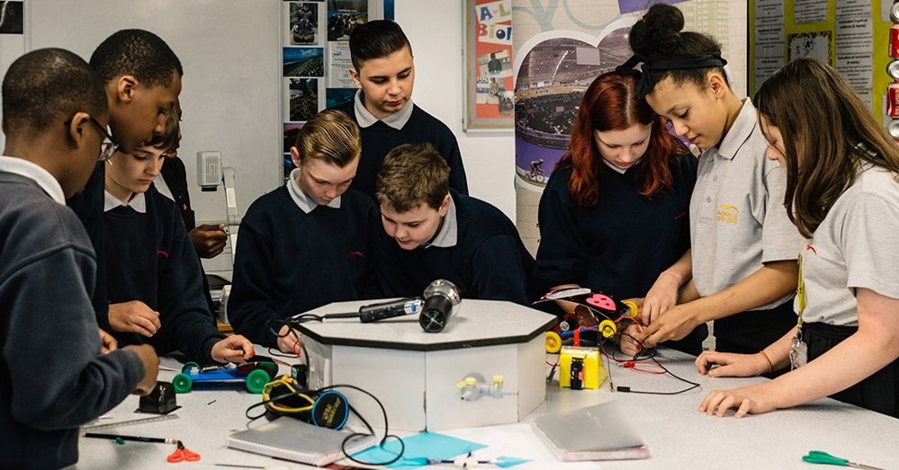 Nine students looking at a range of sensors and robotic toys