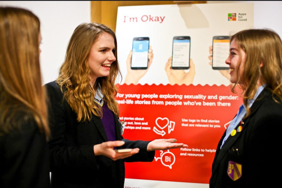 three girls smiling with pop up poster for their app