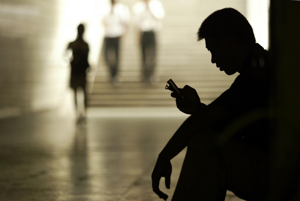 Silhouette of young man sitting on floor by stairs looking at his phone