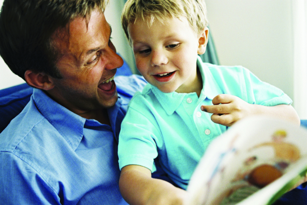 fatrher with a boy sat on his lap with a book, both laughing