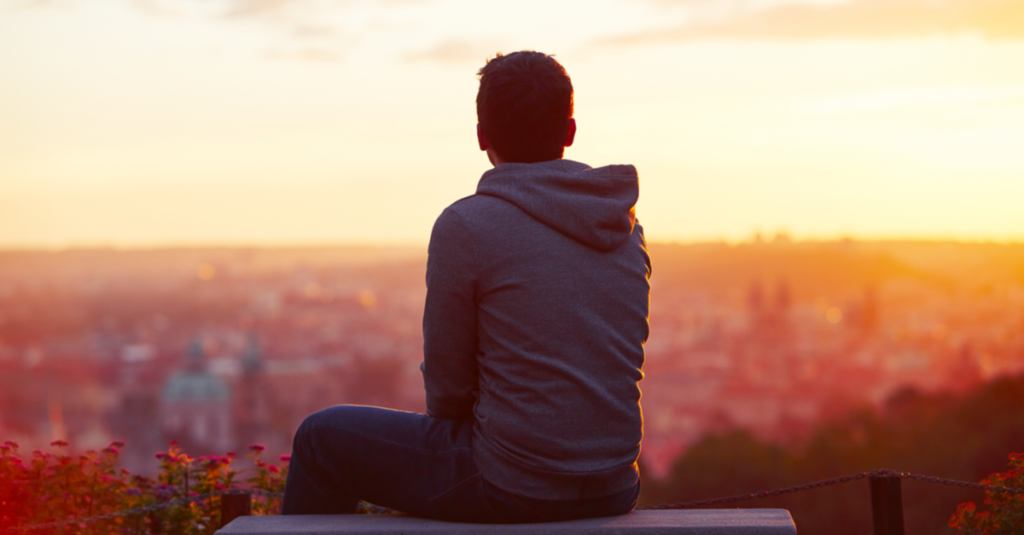 photograph back view of boy wearing a hoodie, looking out over a town at sunset