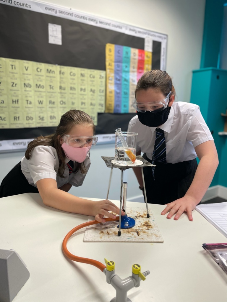 two girls with bunsen burner and flask doing an experiment