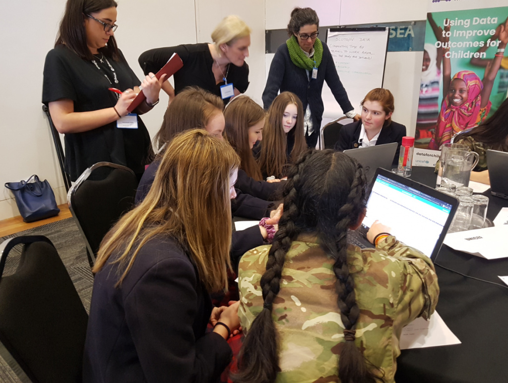 6 girls in school uniform and 3 teachers clustered round 2 laptops