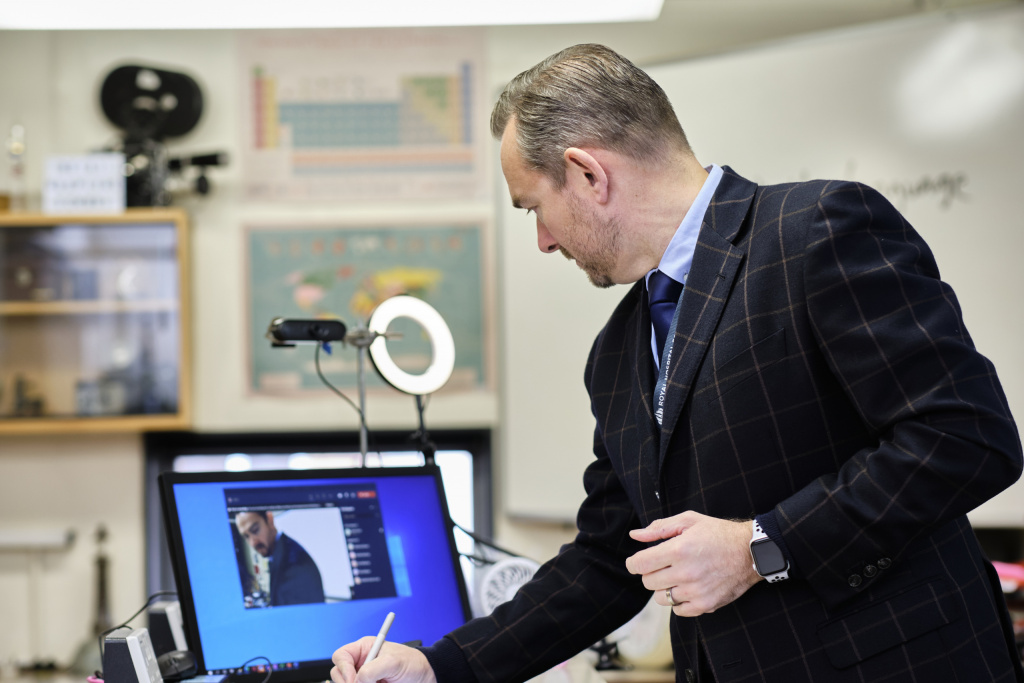 man in suits and tie looking at a screen and adding notes using a pen