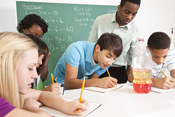 Secondary school students recording experiment results in a science classroom.