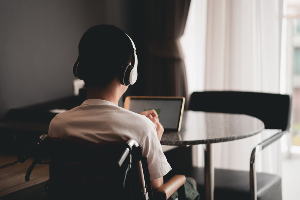 View from behind a young man sitting at a table and using headphones.