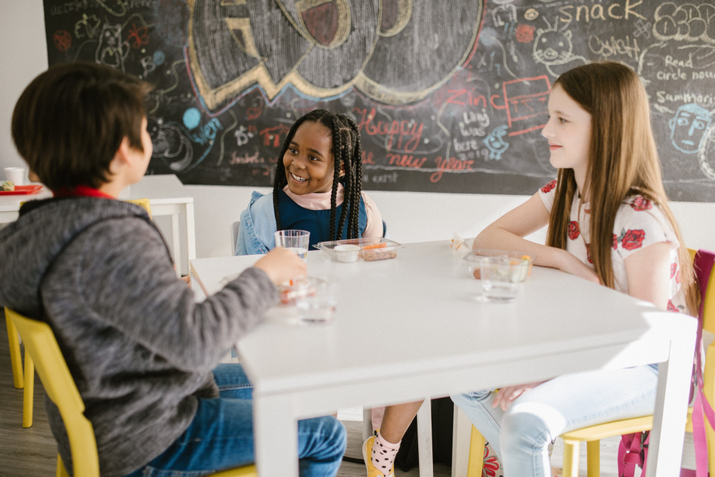 elementary school pupils in a classroom, talking at a table.