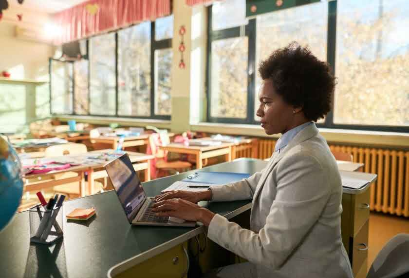 Black female teacher using a laptop at her desk in a classroom