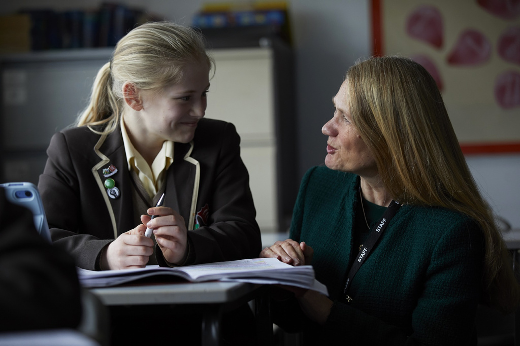 Female secondary school teacher having a conversation with a smiling student.