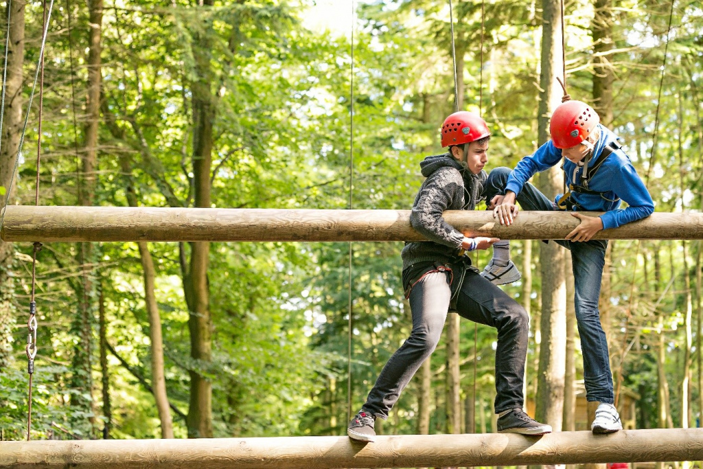 Secondary school boys climbing over suspended posts in a forest.