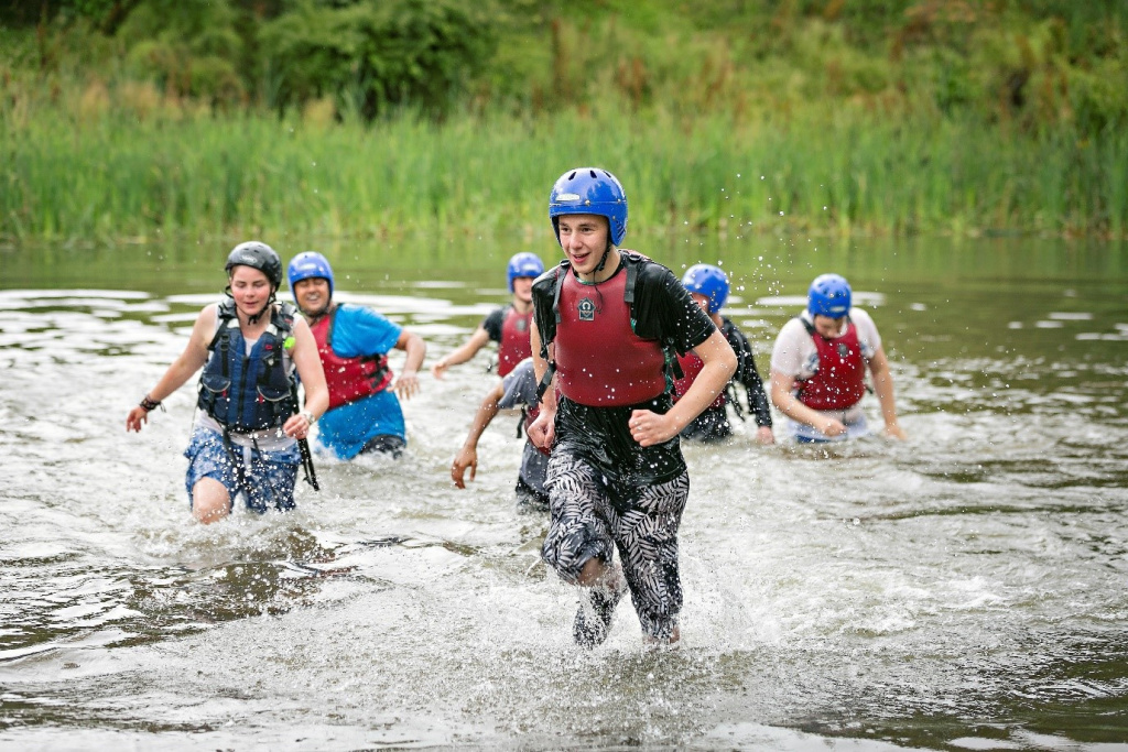 Secondary school students wading through a river.