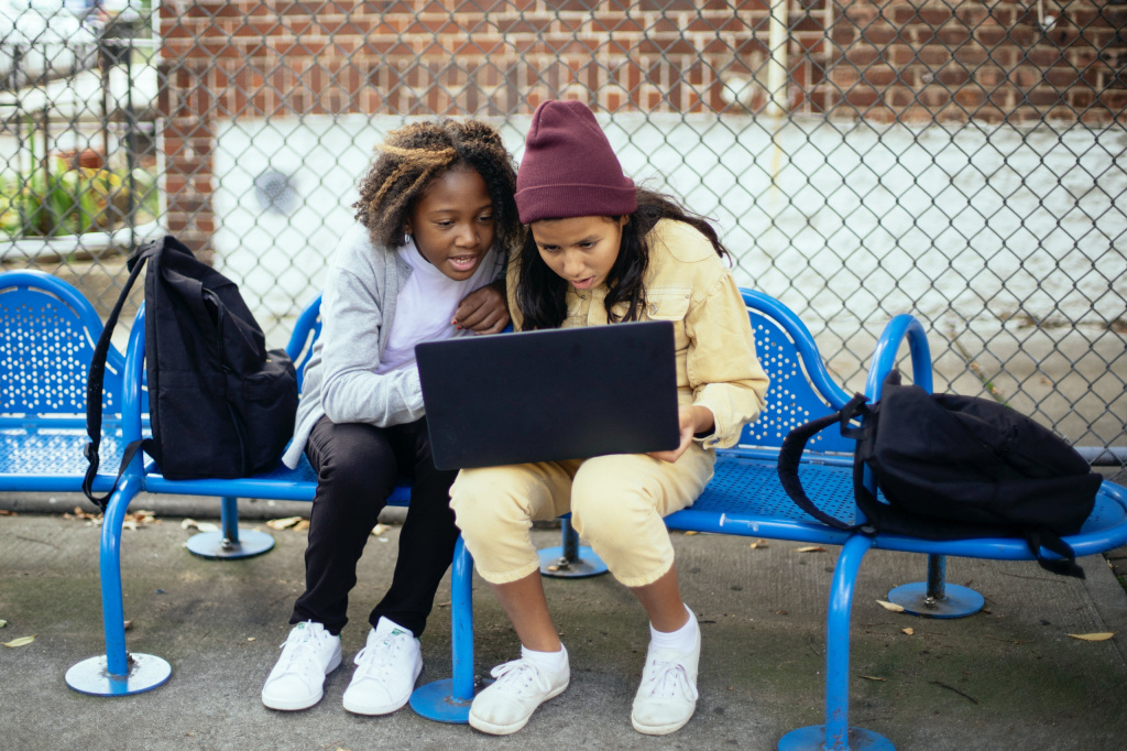 Two secondary school girls looking at a laptop on a bench