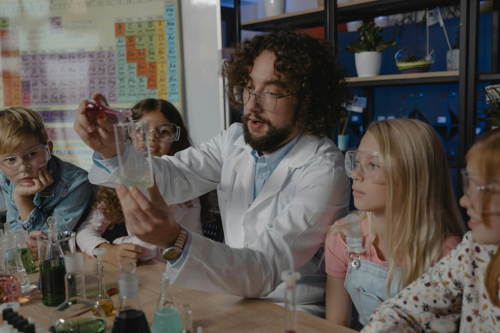 Science teacher with elementary school students pouring liquid into a beaker.