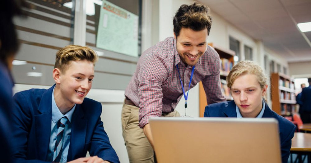 Secondary school Citizenship teacher helping students with a laptop.