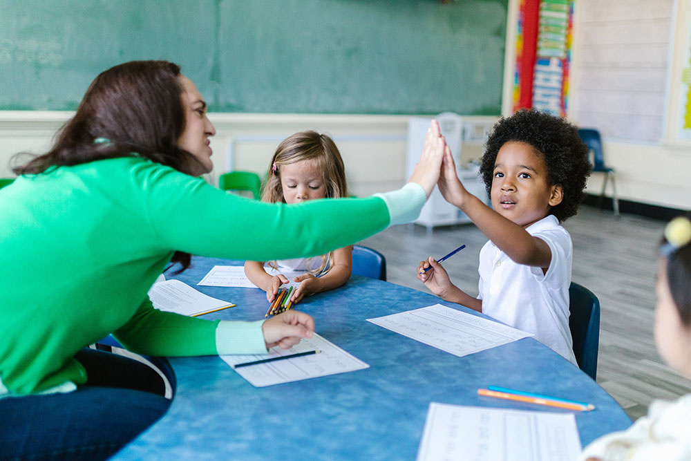 Primary or elementary school teacher high-fiving an autistic pupil in a classroom.