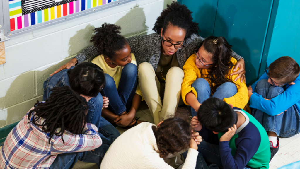 Teacher huddling with students on the classroom floor during an active school shooter lockdown.